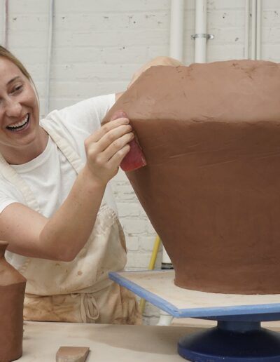 Carlisle Harris with large hand built pot in ISM studio, smoothing with a rubber rib