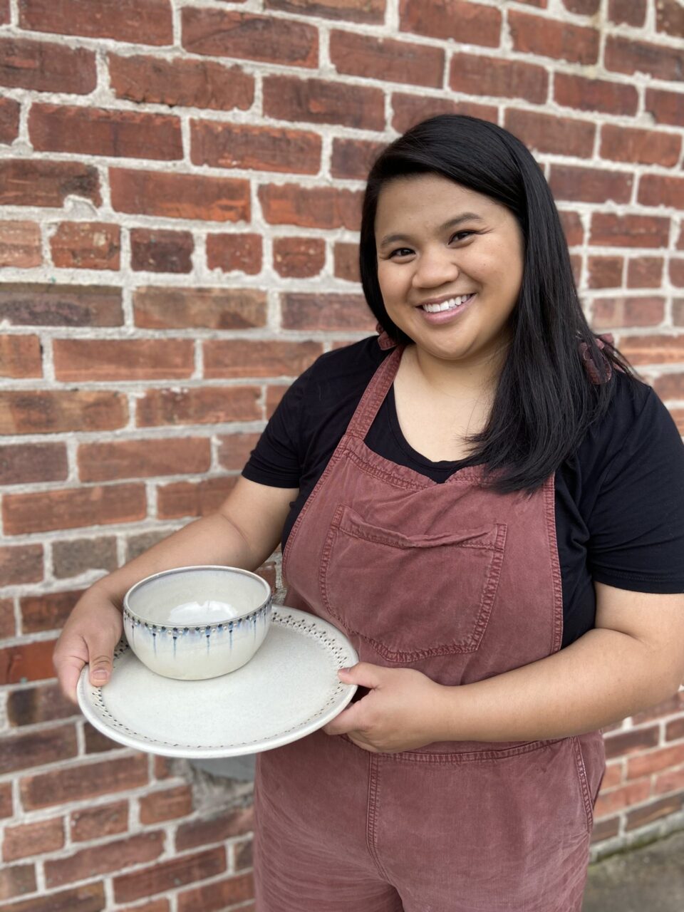 Katie Meili Messersmith holding finished pots, dinner plate and cereal bowl, dot pots