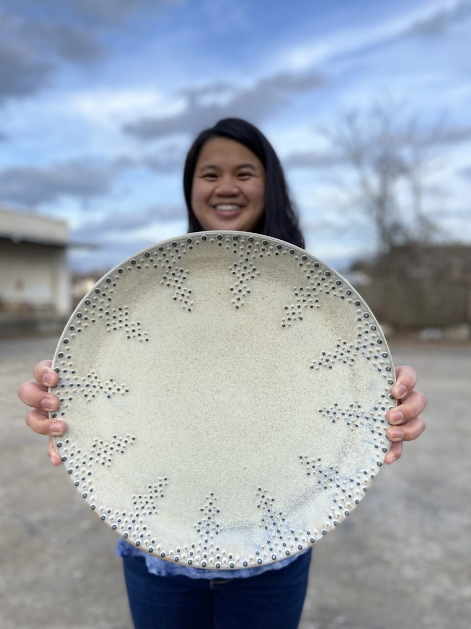Katie Meili Messersmith holding finished pot, dotted serving platter, infinite cobalt whisper pattern