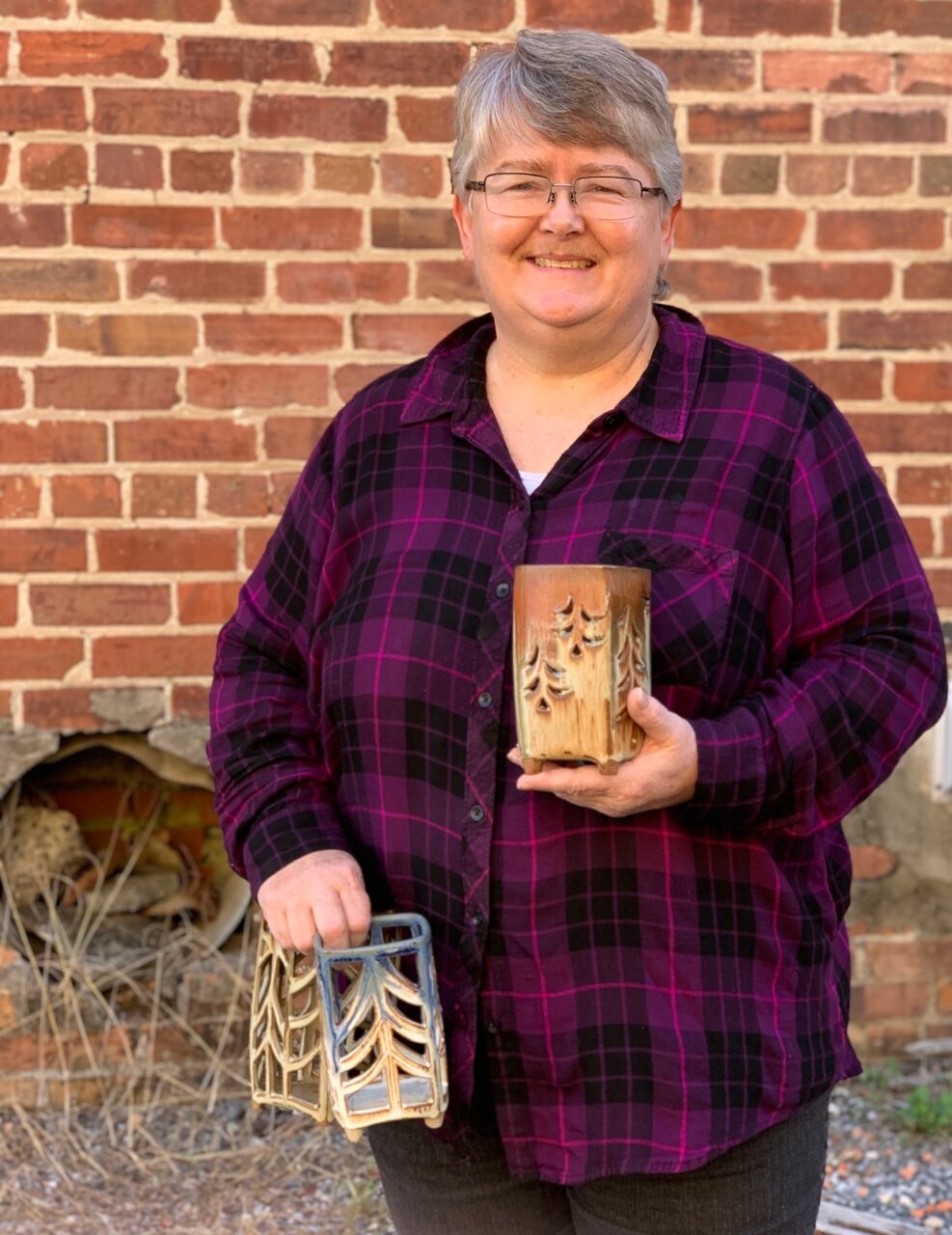 Julia Mann standing, smiling while holding her finished pots, pierced lanterns