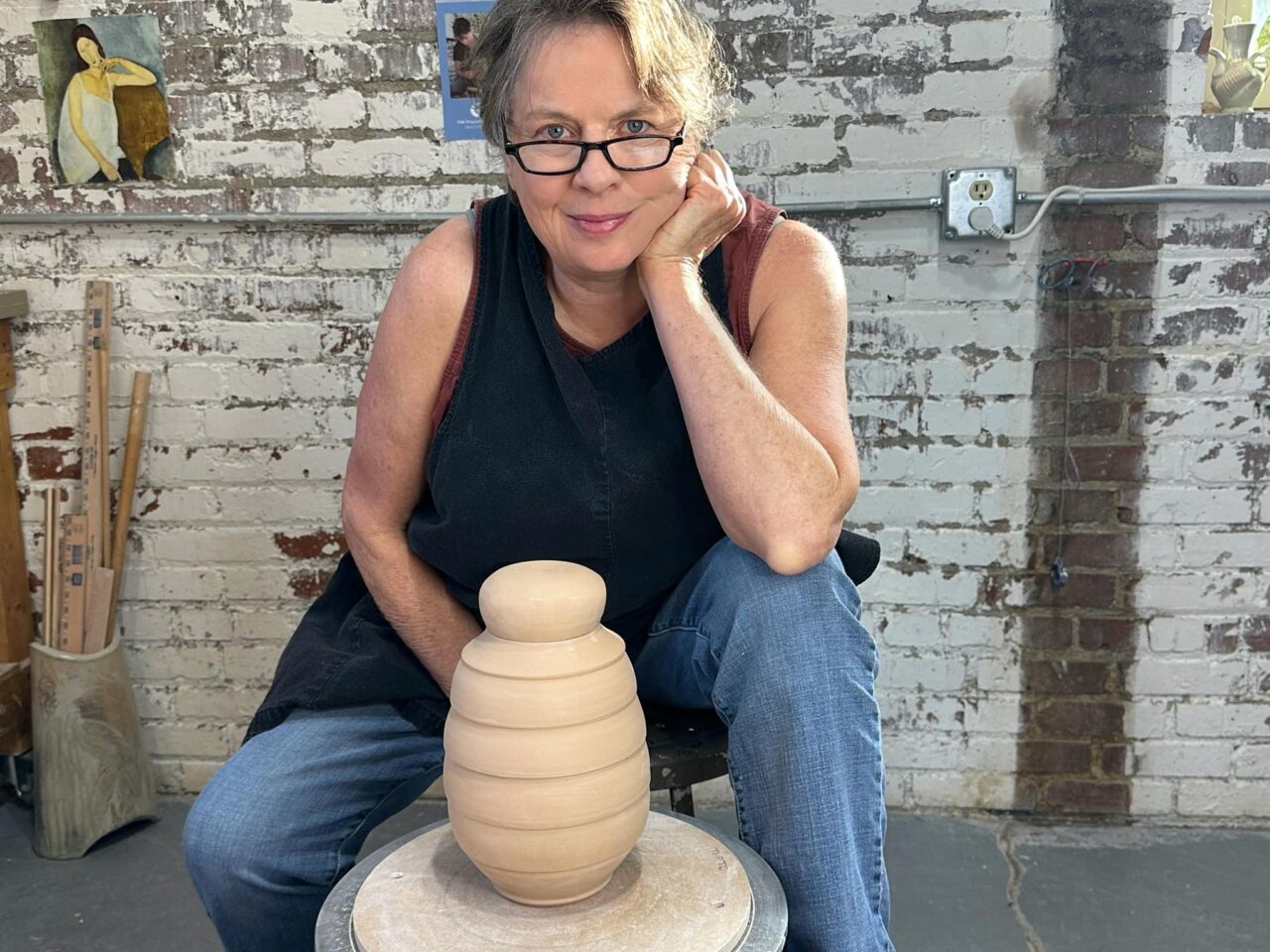 Sarah Wells Rolland sitting at potters wheel with leather hard lidded vessel