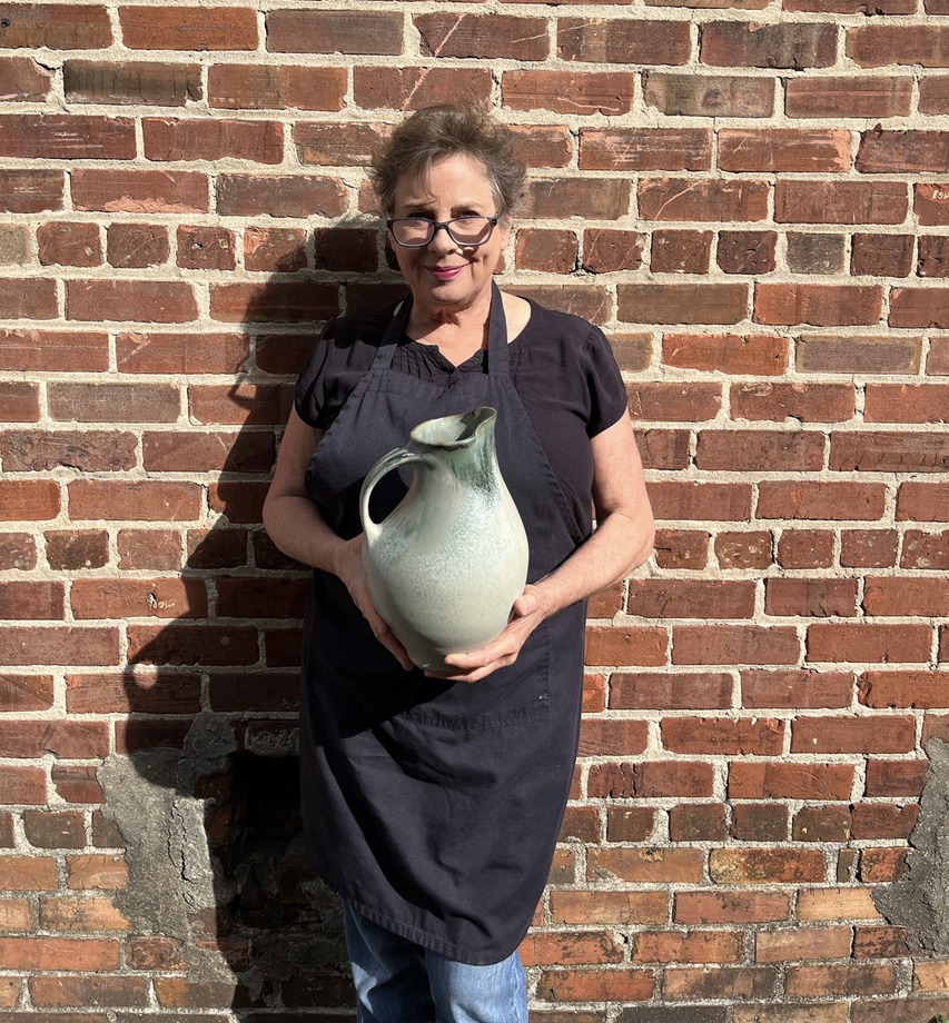 Sarah Wells Rolland holding finished pot, pouring vessel, pitcher, stoney blue glaze