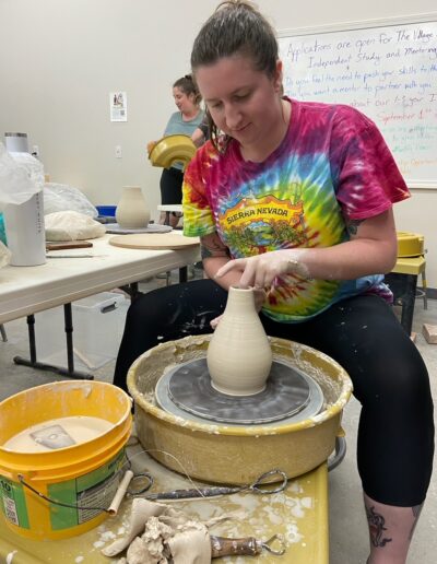 Teaching Center student throwing bottle vase on the potters wheel, collaring, intermediate wheel class