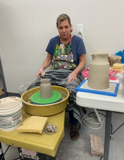Teaching Center student happy throwing vase on potters wheel, intermediate wheel class