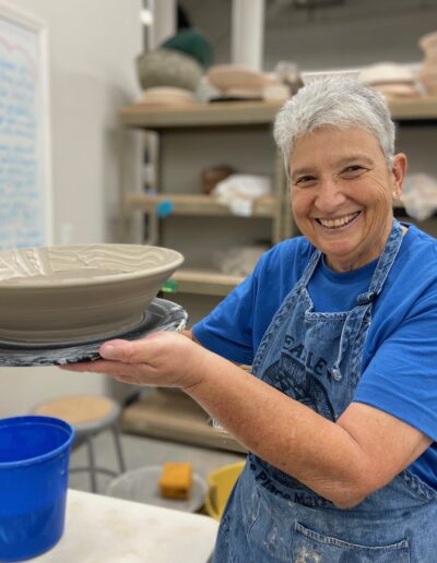 Teaching Center student holding freshly thrown bowl, smiling, intermediate wheel class