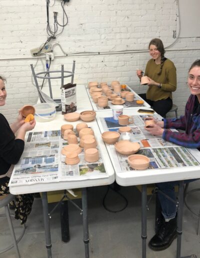 Teaching center students smiling while waxing their pots preparing for glazing, beginning wheel class
