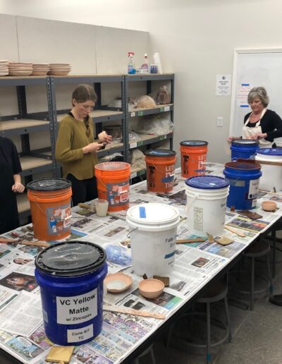 Teaching center students dip glazing in buckets, beginning wheel class