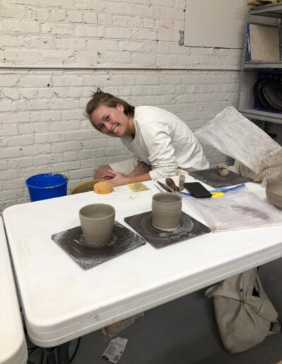 Teaching Center student throwing at potter's wheel with fresh thrown pots next to her, beginning wheel class