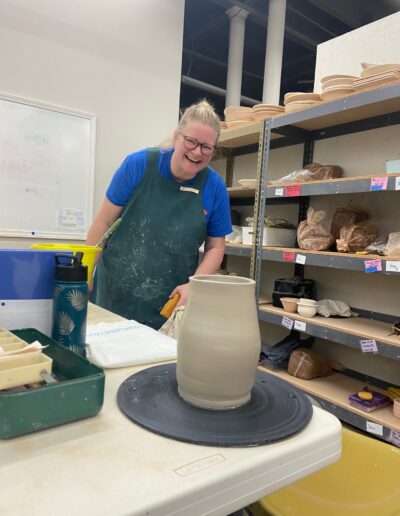 Teaching Center student smiling next to her freshly thrown vase, intermediate wheel class