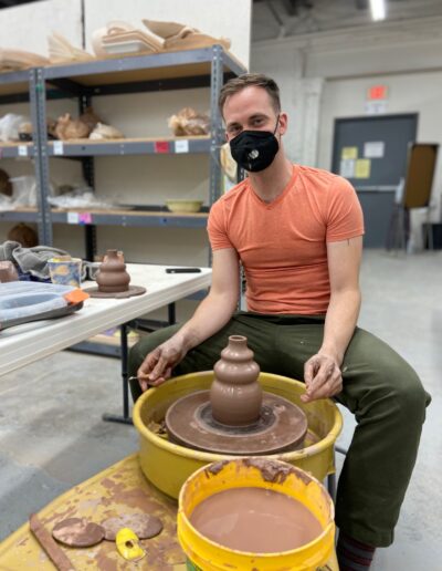 Teaching Center male student happy with freshly thrown vase on the potters wheel, intermediate wheel class